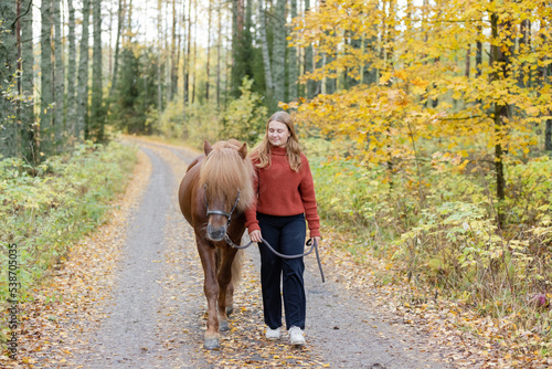 Young woman walking on gravel road with Icelandic horse in autumn scenery. © AnttiJussi