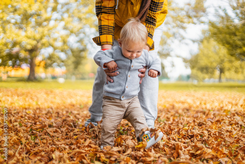 Young mother teaching her little child to walk. Little baby first steps, first autumn, family time concept