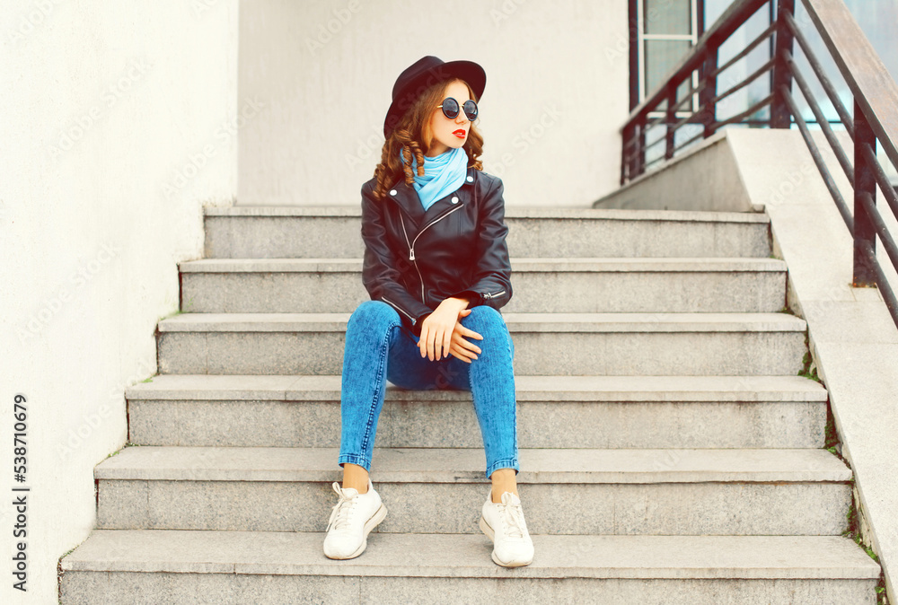Fototapeta premium Portrait of beautiful young woman model wearing black round hat, leather jacket, sunglasses in the city street