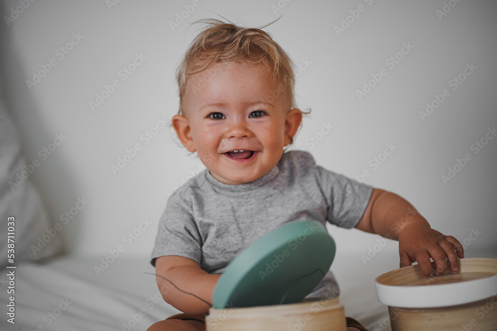 cute happy one year old blond baby boy in casual outfit at home on a cozy sofa smiling or looking into the Camera while open can or box cute happy one year old blond baby boy in casual outfit at home on a cozy sofa smiling or looking into the Camera while open can or box