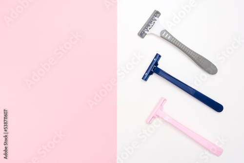 Three disposable razor blades of different colors for removing, shaving unwanted hair on face and body on white and pink background with copy space