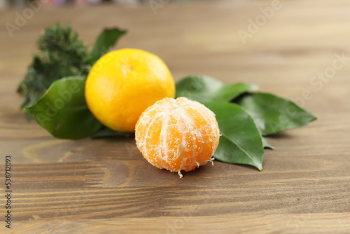 Yellow mandarin or tangerine fruits whole and pilled, green leaves on wooden background, fir tree