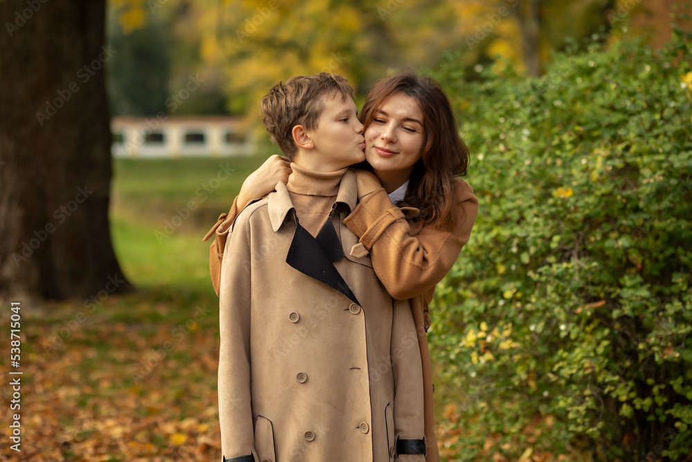 White mom hugs teen age son, child kisses her cheek in beautiful park. Happy motherhood, childhood.Feeling trust and protection. Mothers Day, International Child Protection Day. Horizontal plane White mom hugs teen age son, child kisses her cheek in beautiful park. Happy motherhood, childhood.Feeling trust and protection. Mothers Day, International Child Protection Day. Horizontal plane