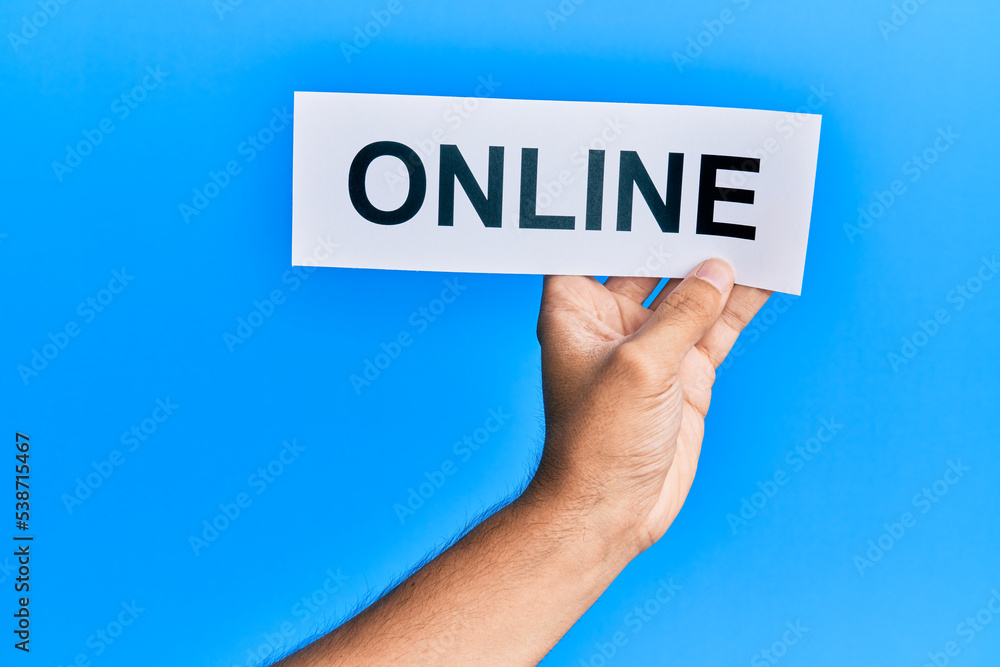 Hand of caucasian man holding paper with online word over isolated blue background Hand of caucasian man holding paper with online word over isolated blue background