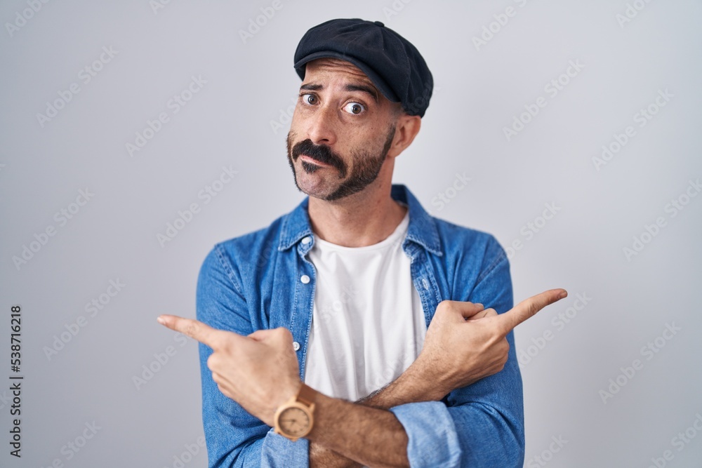Hispanic man with beard standing over isolated background pointing to both sides with fingers, different direction disagree Hispanic man with beard standing over isolated background pointing to both sides with fingers, different direction disagree