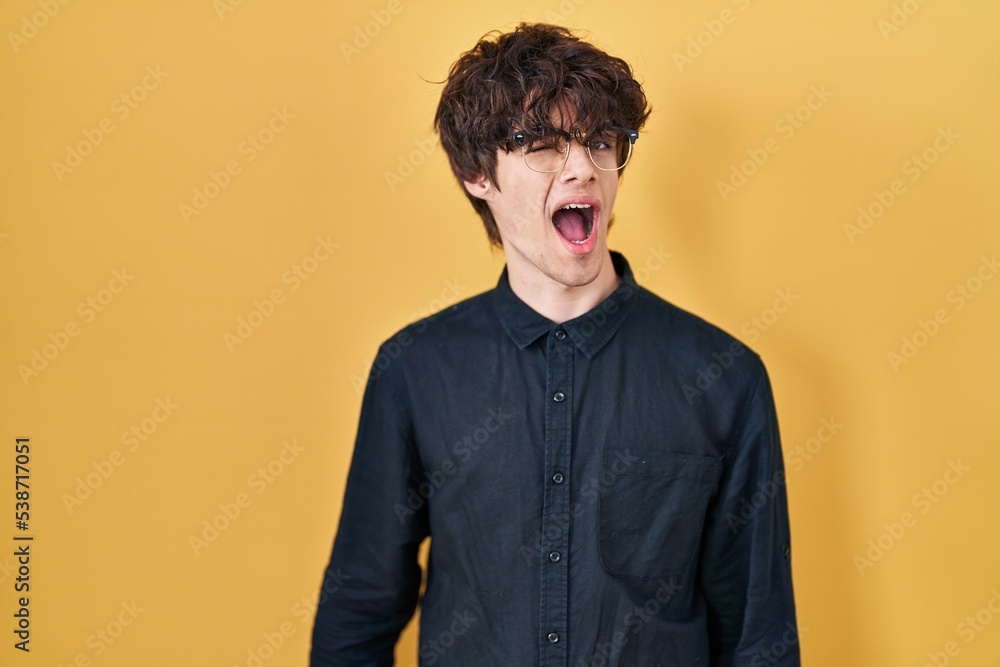 Young man wearing glasses over yellow background winking looking at the camera with sexy expression, cheerful and happy face. Young man wearing glasses over yellow background winking looking at the camera with sexy expression, cheerful and happy face.