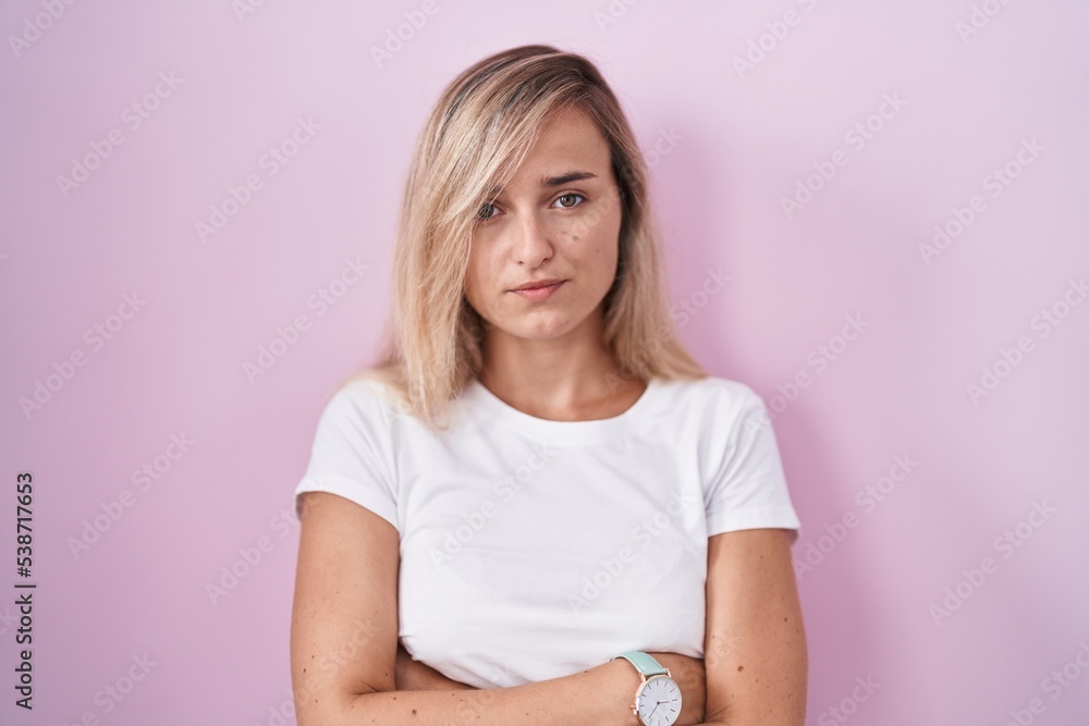 Young blonde woman standing over pink background skeptic and nervous, disapproving expression on face with crossed arms. negative person. Young blonde woman standing over pink background skeptic and nervous, disapproving expression on face with crossed arms. negative person.