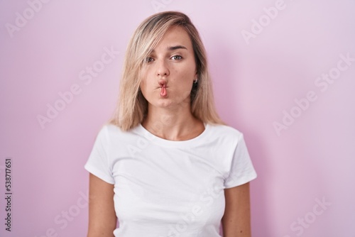 Young blonde woman standing over pink background making fish face with lips, crazy and comical gesture. funny expression.