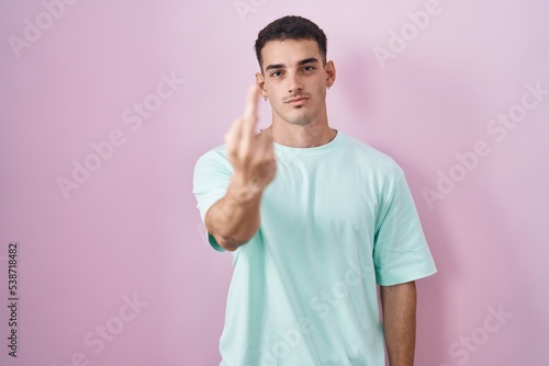 Handsome hispanic man standing over pink background showing middle finger, impolite and rude fuck off expression