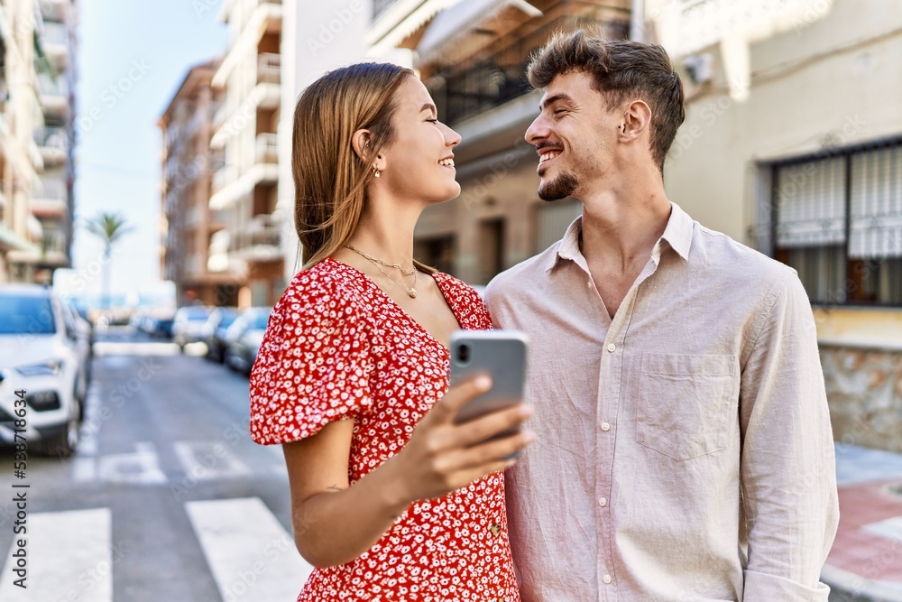 Young hispanic couple smiling happy and using smartphone at the city.