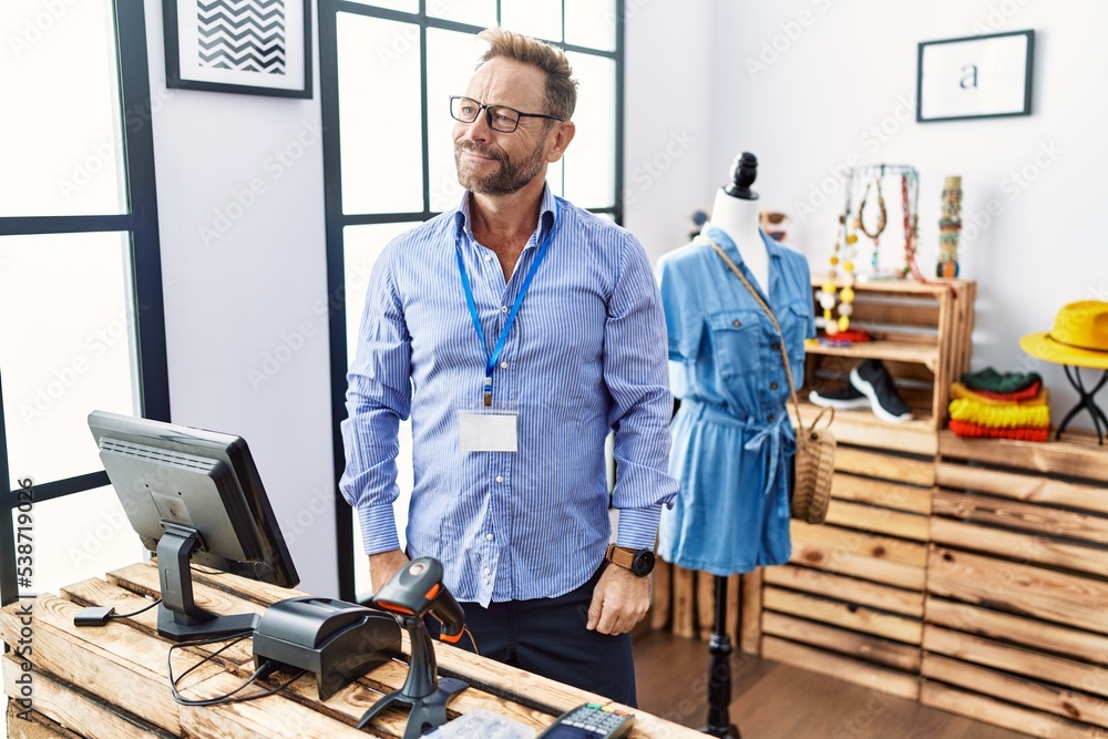 Middle age man working as manager at retail boutique smiling looking to the side and staring away thinking.