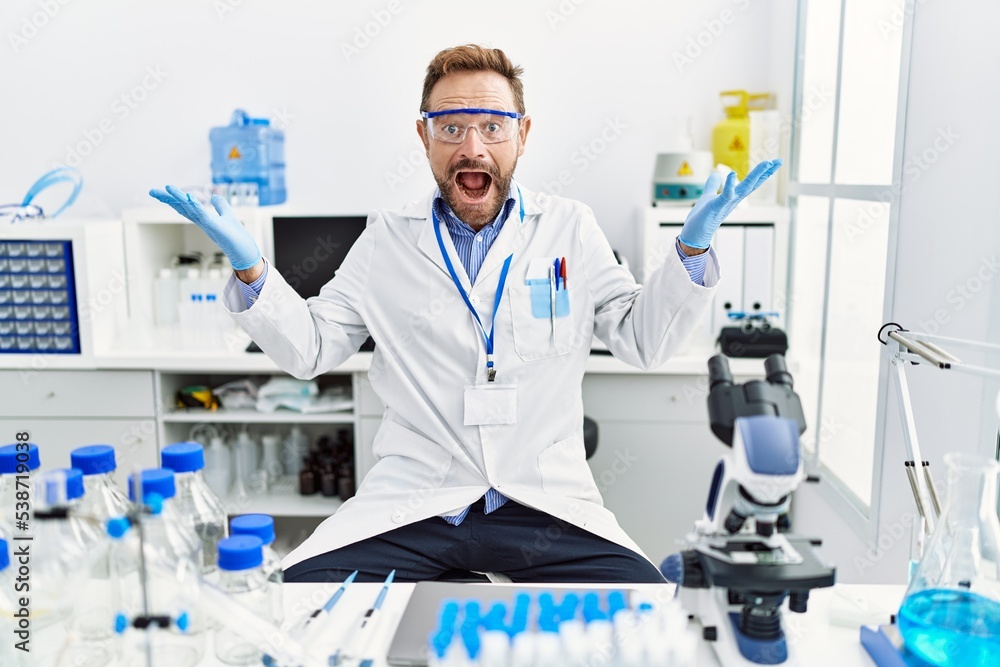 Middle age man working at scientist laboratory celebrating victory with happy smile and winner expression with raised hands Middle age man working at scientist laboratory celebrating victory with happy smile and winner expression with raised hands