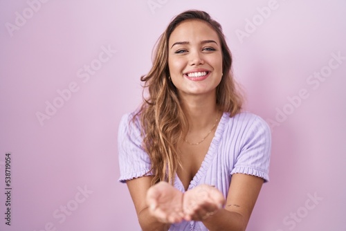 Young hispanic woman standing over pink background smiling with hands palms together receiving or giving gesture. hold and protection
