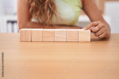 Young beautiful hispanic woman business worker sitting on table with wooden cubes at office