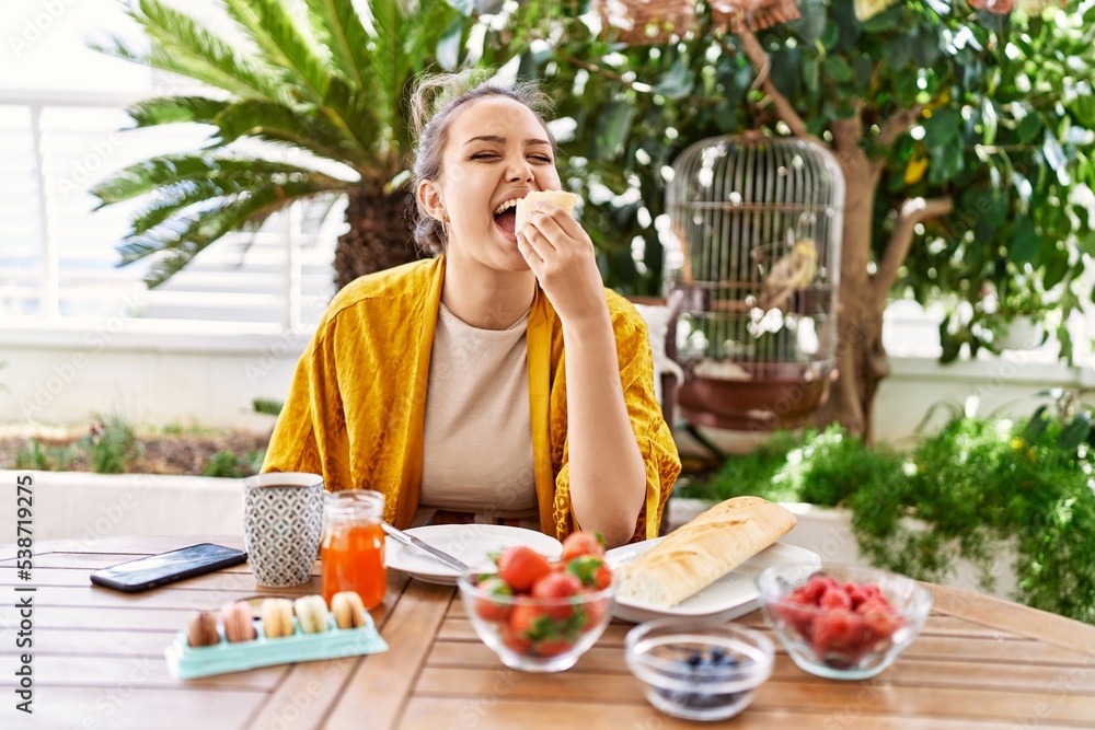 Young hispanic girl having breakfast sitting on the table at terrace.