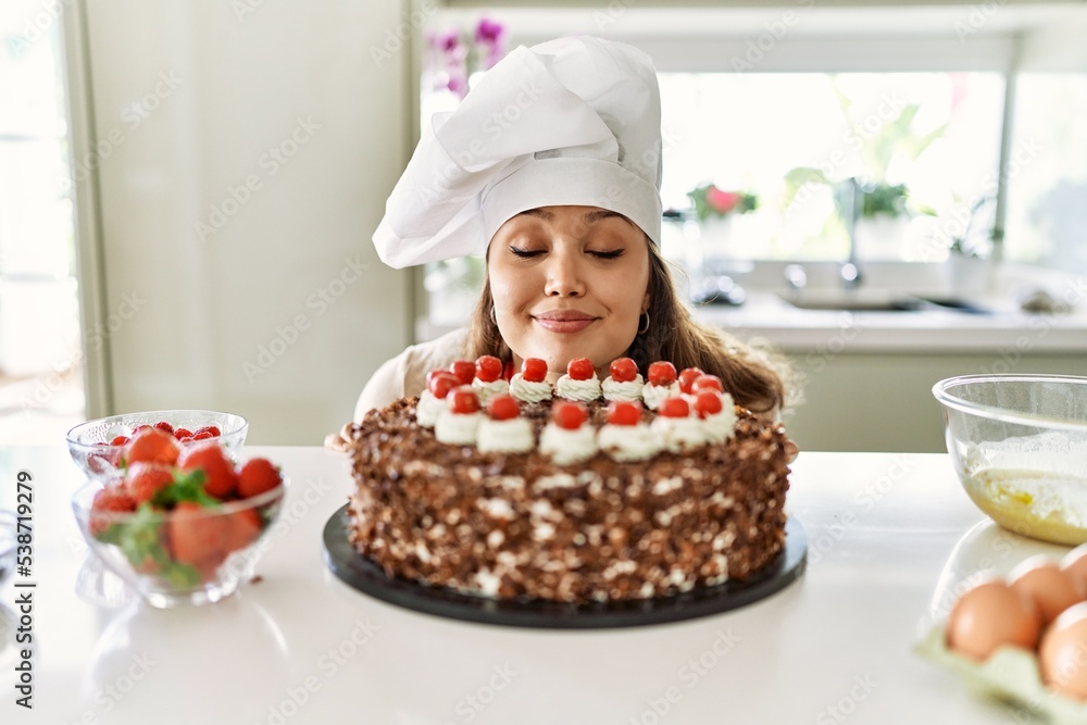 Young beautiful hispanic woman smiling confident smelling cake at the kitchen Young beautiful hispanic woman smiling confident smelling cake at the kitchen