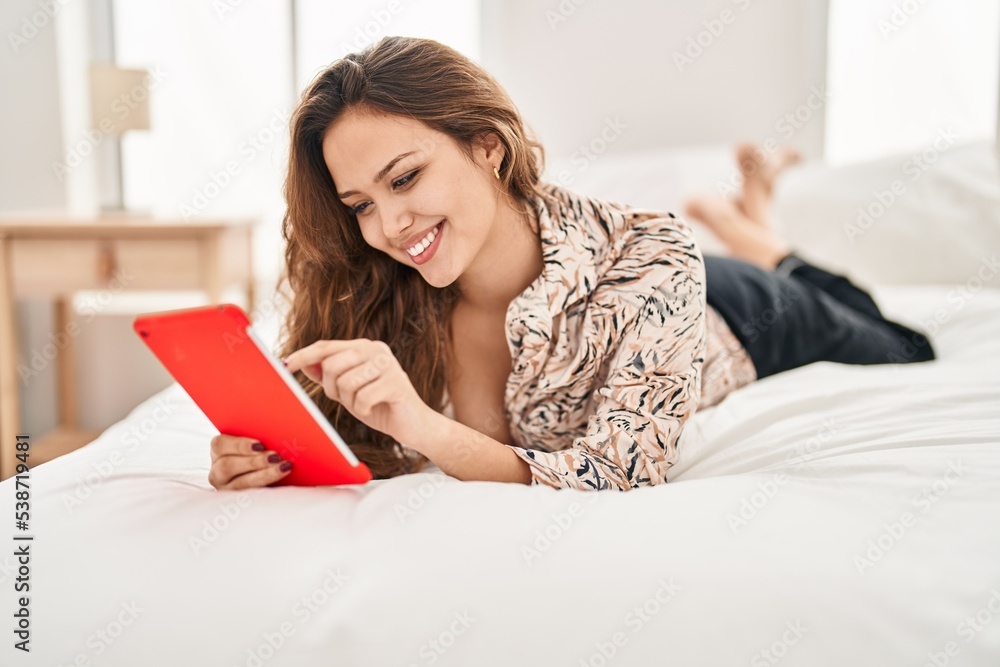 Young beautiful hispanic woman using touchpad lying on bed at bedroom