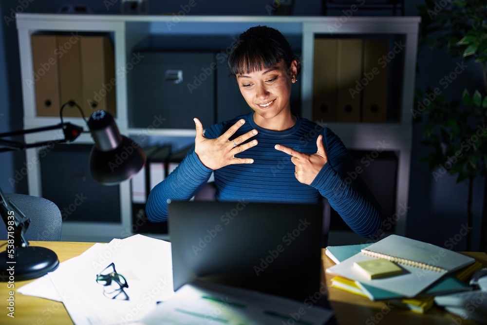 Young beautiful woman working at the office at night showing and pointing up with fingers number seven while smiling confident and happy. Young beautiful woman working at the office at night showing and pointing up with fingers number seven while smiling confident and happy.