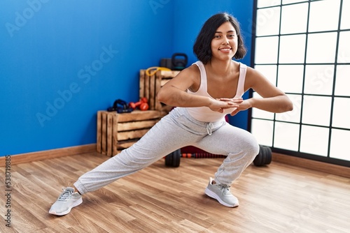 Young latin woman smiling confident stretching at sport center