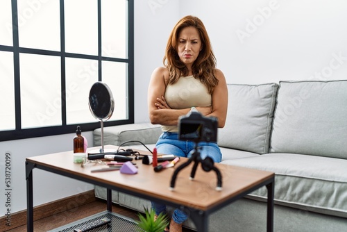 Middle age hispanic woman recording make up tutorial with smartphone at home skeptic and nervous, disapproving expression on face with crossed arms. negative person.