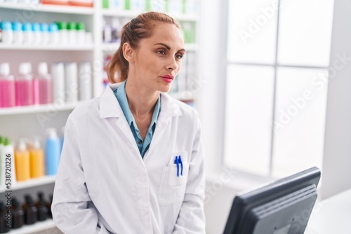 Young beautiful hispanic woman pharmacist using computer with serious expression at pharmacy