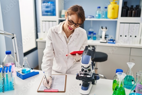 Young caucasian woman wearing scientist uniform using touchpad working at laboratory