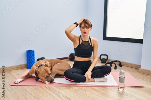Young beautiful woman sitting on yoga mat confuse and wondering about question. uncertain with doubt, thinking with hand on head. pensive concept.