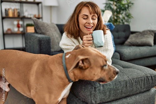 Young caucasian woman drinking coffee lying on sofa with dog at home