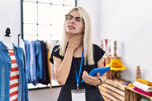 Young blonde woman working as manager at retail boutique touching painful neck, sore throat for flu, clod and infection