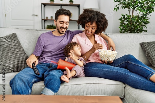 Couple and daughter watching movie sitting on sofa at home