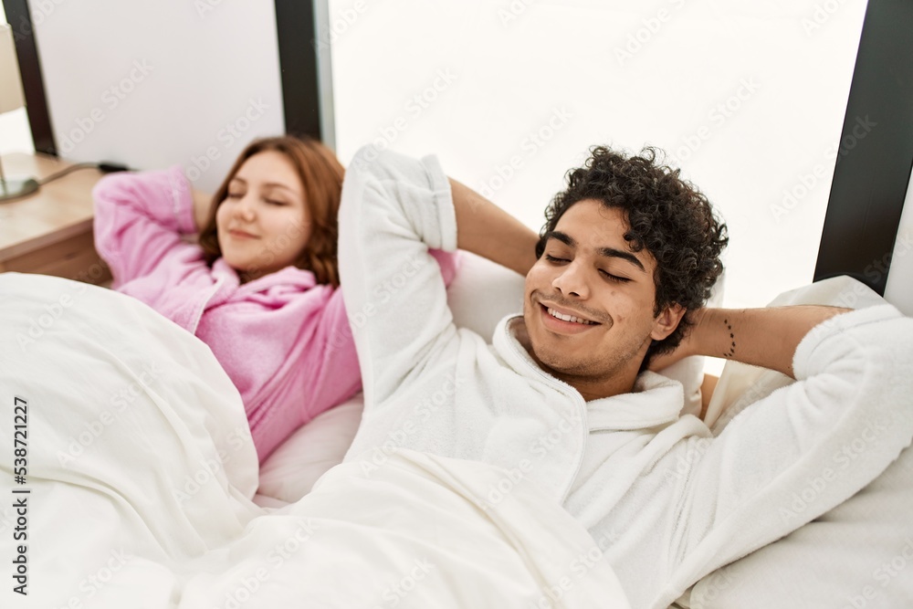 Young couple smiling happy relaxed with hands on head lying on the bed at bedroom. Young couple smiling happy relaxed with hands on head lying on the bed at bedroom.
