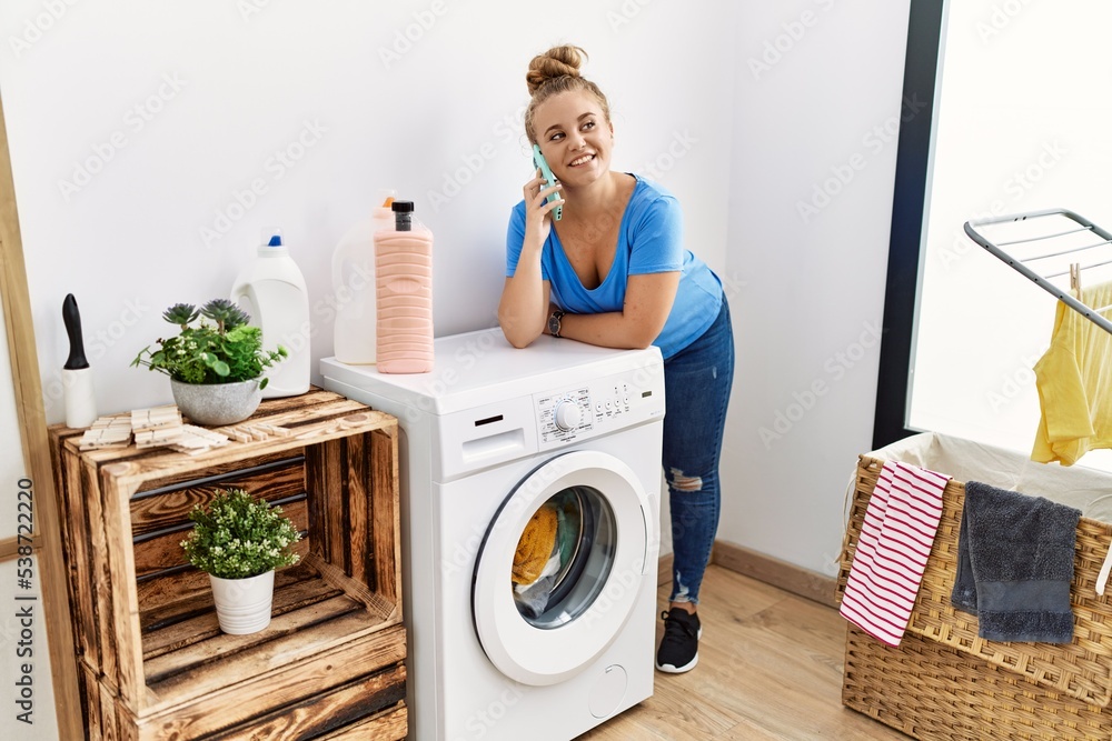 Young blonde girl talking on the smartphone waiting for washing machine at laundry room Young blonde girl talking on the smartphone waiting for washing machine at laundry room