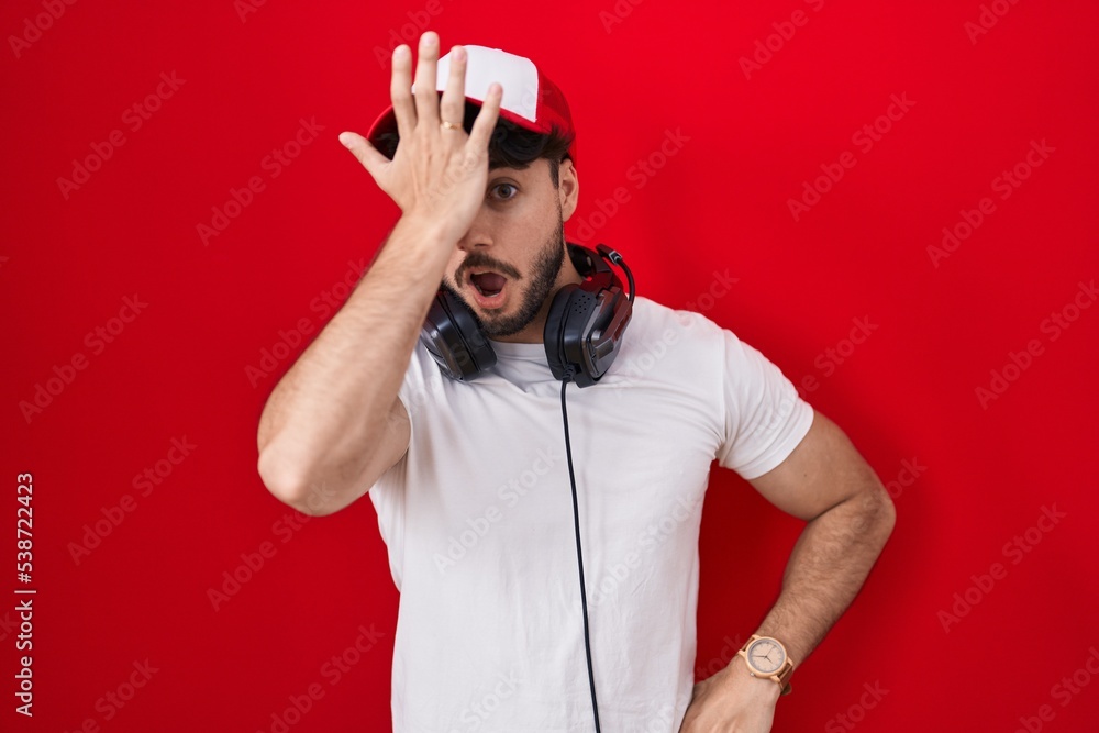 Hispanic man with beard wearing gamer hat and headphones surprised with hand on head for mistake, remember error. forgot, bad memory concept. Hispanic man with beard wearing gamer hat and headphones surprised with hand on head for mistake, remember error. forgot, bad memory concept.