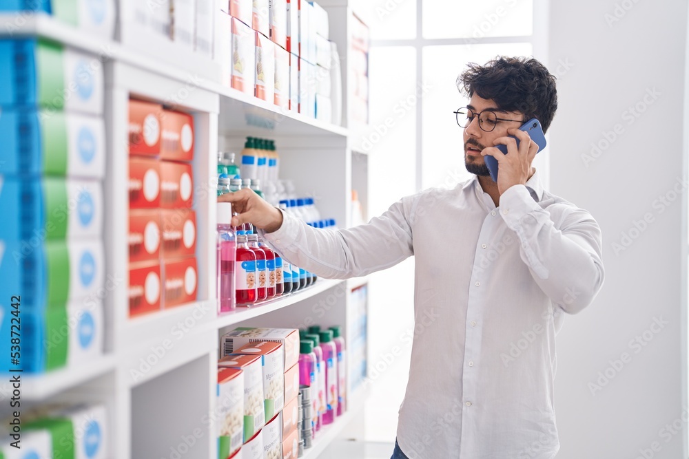 Young hispanic man client talking on smartphone at pharmacy