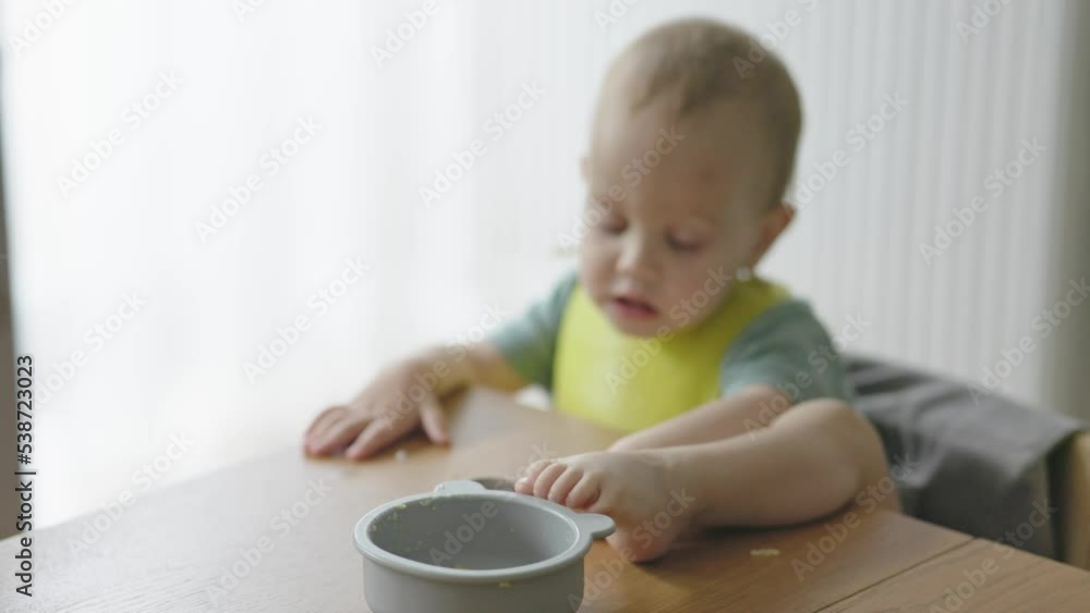 toddler baby child put leg on table while eating lunch learning feed itself feeding concept kid's behavior at kitchen table. caucasian cute baby kid trying to take plate using foot. playing with food toddler baby child put leg on table while eating lunch learning feed itself feeding concept kid's behavior at kitchen table. caucasian cute baby kid trying to take plate using foot. playing with food