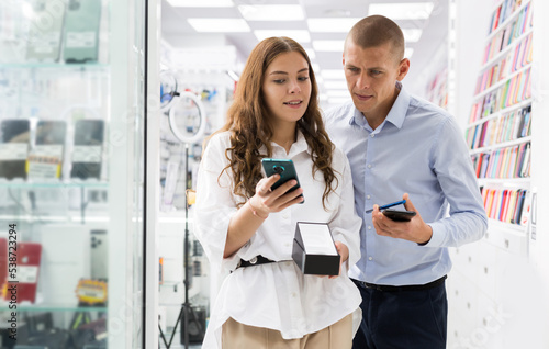 Young attractive woman buyer and man choosing new smart phones in consumer electronics store