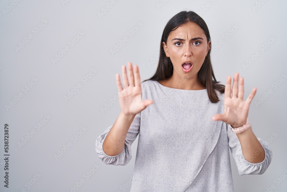 Young hispanic woman standing over white background doing stop gesture with hands palms, angry and frustration expression