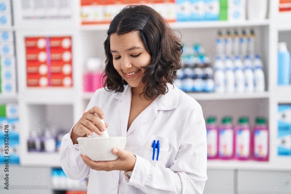 Young woman pharmacist smiling confident mixing medicine at pharmacy