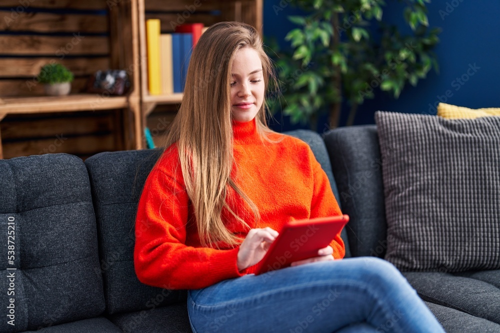 Young blonde woman using touchpad sitting on sofa at home Young blonde woman using touchpad sitting on sofa at home