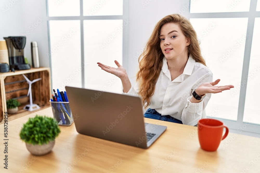 Young caucasian woman working at the office using computer laptop clueless and confused expression with arms and hands raised. doubt concept. Young caucasian woman working at the office using computer laptop clueless and confused expression with arms and hands raised. doubt concept.