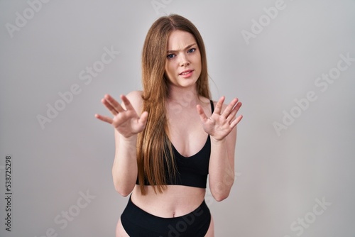 Young caucasian woman wearing lingerie afraid and terrified with fear expression stop gesture with hands, shouting in shock. panic concept.