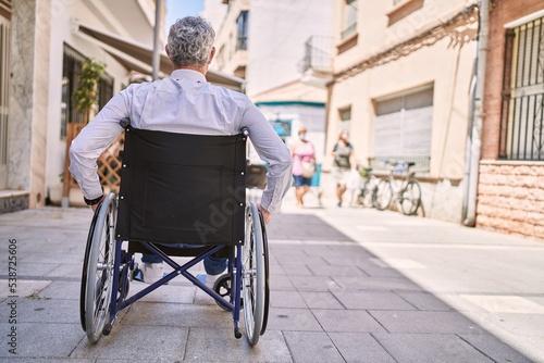 Middle age hispanic man wearing business clothes sitting on wheelchair at street