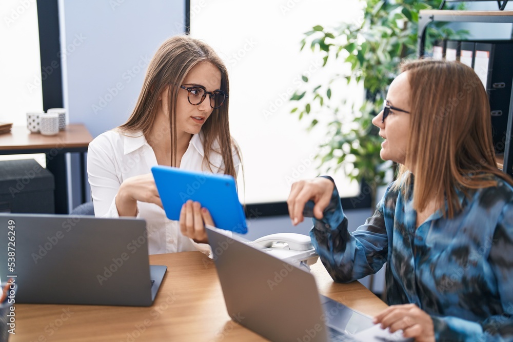 Two women business workers using laptop and touchpad working at office Two women business workers using laptop and touchpad working at office