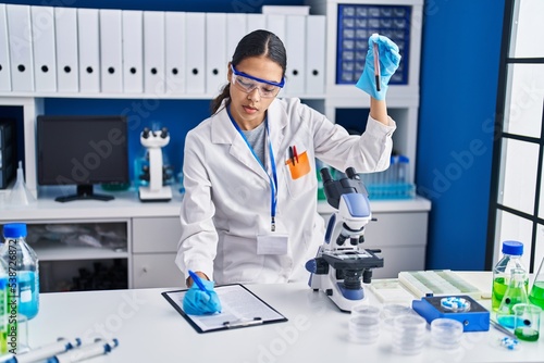 Young african american woman scientist analysing blood test tube writing report at laboratory