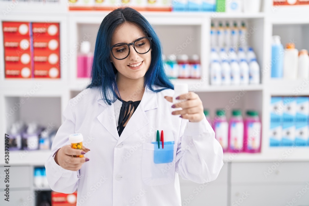 Young caucasian woman pharmacist smiling confident holding pills bottles at pharmacy