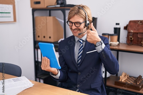 Caucasian man with mustache wearing call center agent headset smiling happy and positive, thumb up doing excellent and approval sign