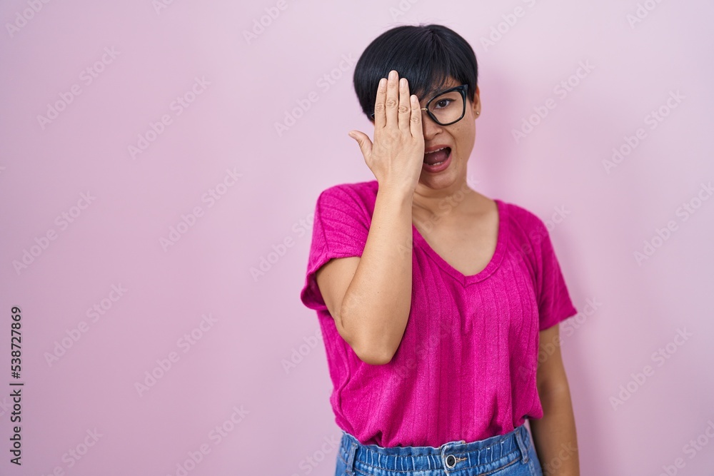 Young asian woman with short hair standing over pink background covering one eye with hand, confident smile on face and surprise emotion. Young asian woman with short hair standing over pink background covering one eye with hand, confident smile on face and surprise emotion.