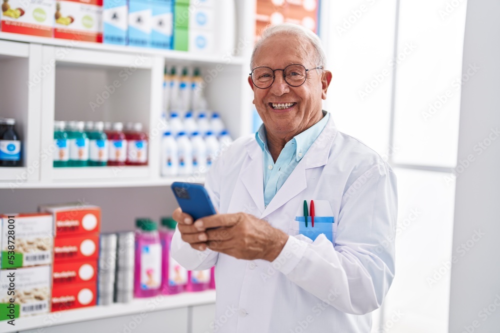 Senior grey-haired man pharmacist using smartphone at pharmacy