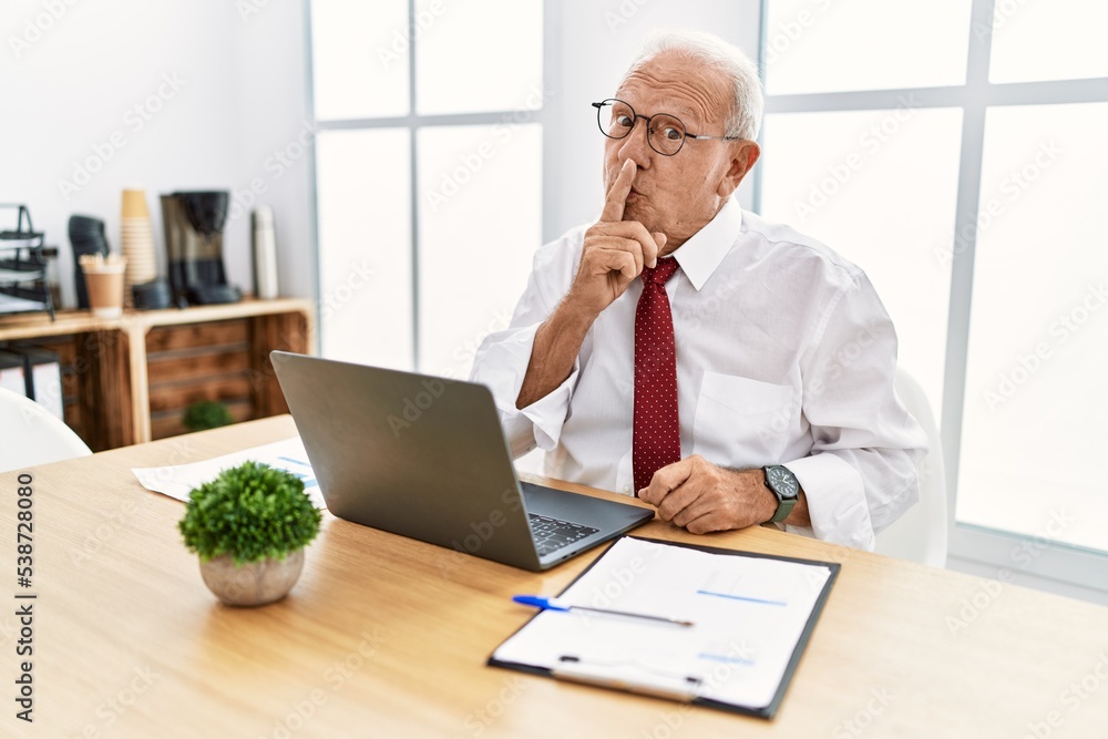 Senior man working at the office using computer laptop asking to be quiet with finger on lips. silence and secret concept. Senior man working at the office using computer laptop asking to be quiet with finger on lips. silence and secret concept.