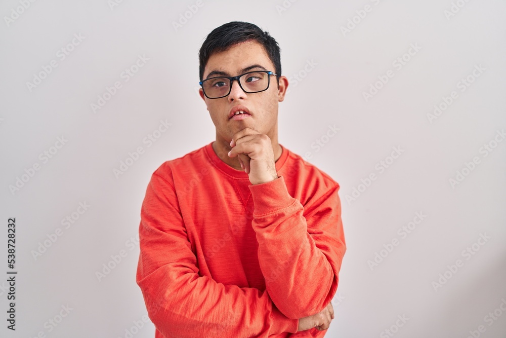 Young hispanic man with down syndrome standing over white background smiling looking confident at the camera with crossed arms and hand on chin. thinking positive. Young hispanic man with down syndrome standing over white background smiling looking confident at the camera with crossed arms and hand on chin. thinking positive.